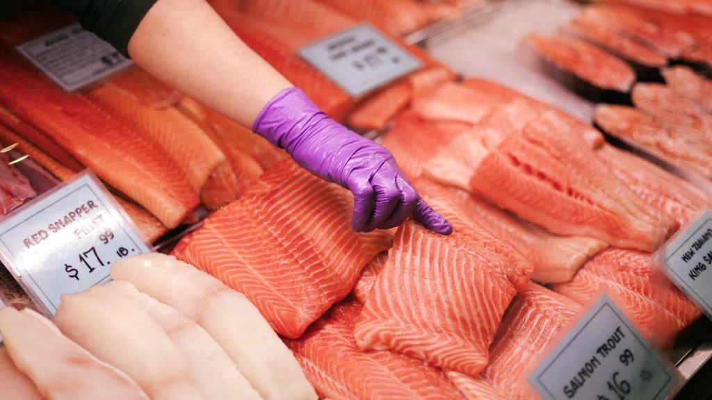 Un vendedor escoge un trozo de salmón entre numerosos pescados, lo que demuestra el cuidadoso proceso de selección y la abundancia de opciones.